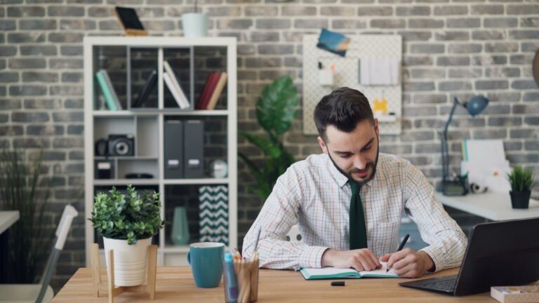 Businessman writing in notebook at modern office setup